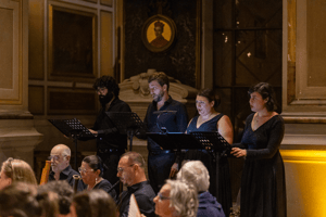 Quattro cantanti, due uomini e due donne, eseguono un brano di musica sacra accompagnati da un ensemble strumentale, sullo sfondo l’altare riccamente decorato.