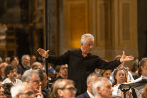 Il direttore d’orchestra dirige con intensità, le mani alzate a guidare il coro e i musicisti nella chiesa gremita.