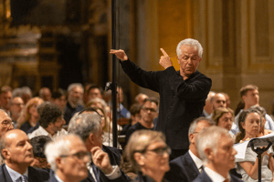 Il direttore d’orchestra dirige con le mani sollevate e sguardo intenso, immerso nella musica sacra.
