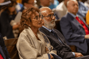 Primo piano di una coppia di spettatori seduti in prima fila, che ascoltano con attenzione il concerto in un’atmosfera raccolta e solenne.
