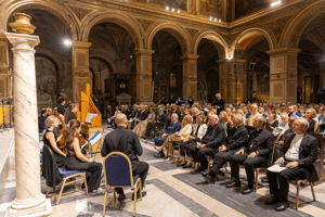 Vista d’insieme della chiesa gremita di pubblico durante il Concerto di Musica Sacra, con il relatore che parla davanti ai musicisti e ai coristi.