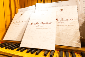 Partiture della “Messa Papa Benedetto XIII a 16 voci” di Giuseppe Ottavio Pitoni appoggiate su una tastiera d’organo, illuminate da una luce calda.