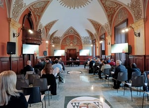 Vista frontale della sala durante la conferenza “Paesaggi dell’anima”, con i relatori al tavolo principale e il pubblico seduto ai lati, sotto eleganti volte affrescate. Sugli schermi, il titolo dell’incontro.