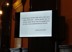Il Prof. Gabriele Sani in piedi al centro della sala conferenze mentre parla al pubblico, con due schermi che mostrano un testo storico attribuito all’Arcivescovo di Manfredonia.