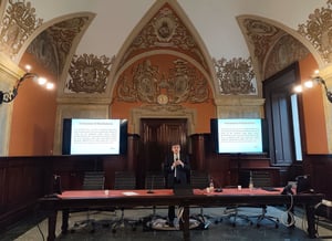 Il Prof. Gabriele Sani in piedi al centro della sala conferenze mentre parla al pubblico, con due schermi che mostrano un testo storico attribuito all’Arcivescovo di Manfredonia