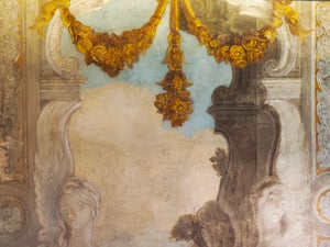Affresco con decorazioni architettoniche: una ghirlanda dorata di fiori e frutti pende al centro su sfondo azzurro; ai lati, figure femminili scolpite in chiaroscuro
