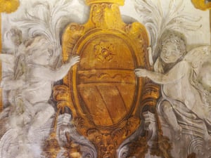 Affresco raffigurante uno stemma araldico dorato e scolpito, con decorazioni barocche; due putti alati ai lati sostengono lo scudo, circondato da volute ornamentali